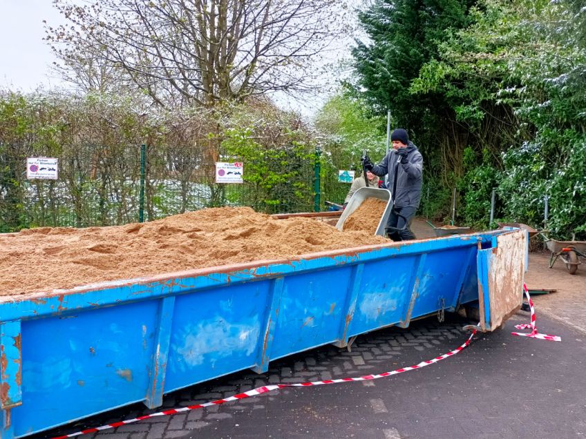 Mann kippt Schubkarre mit Sand in den Container aus