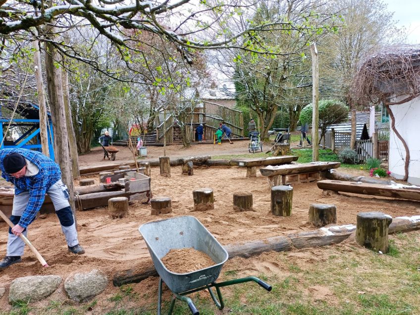 Mann schippt Sand aus Sandkasten in Schubkarre